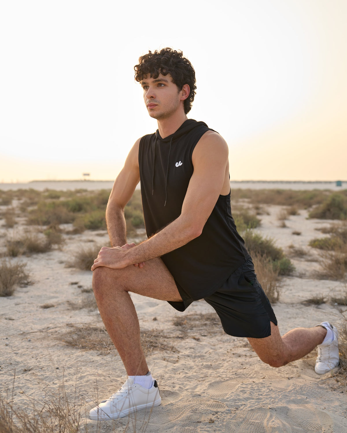 Man in the Urthlete black sleeveless hoodie doing a lunge stretch in the desert