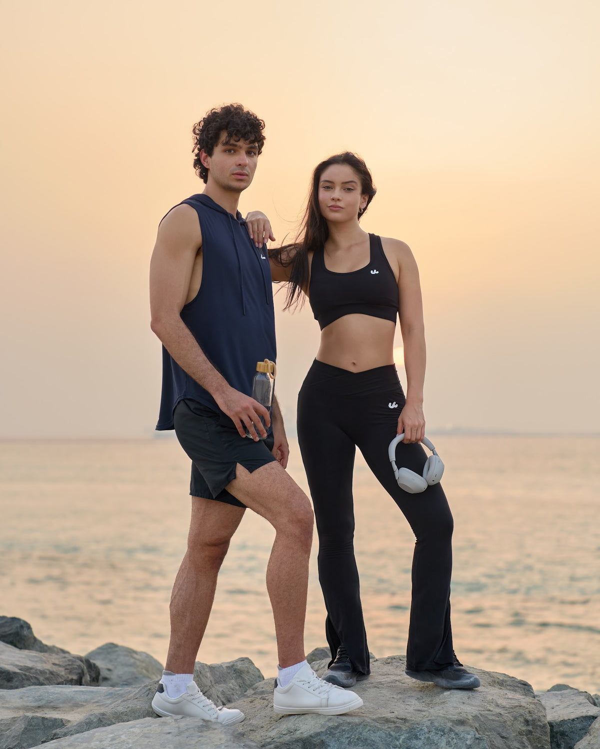 Man and woman standing on rocks by the sea at sunset in Urthlete activewear