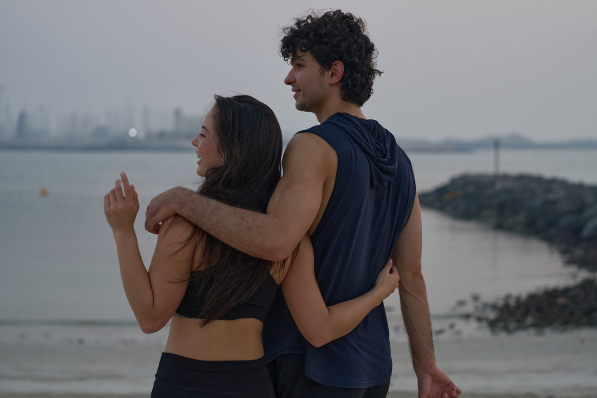 Couple by the sea in Urthlete activewear, woman in the sports bra and man in the sleeveless hoodie