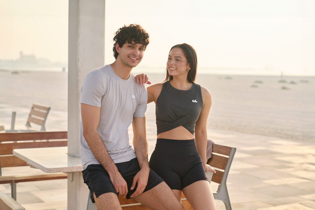 Man in the Urthlete muscle tee and woman in the fitted tank at a beachside cafe