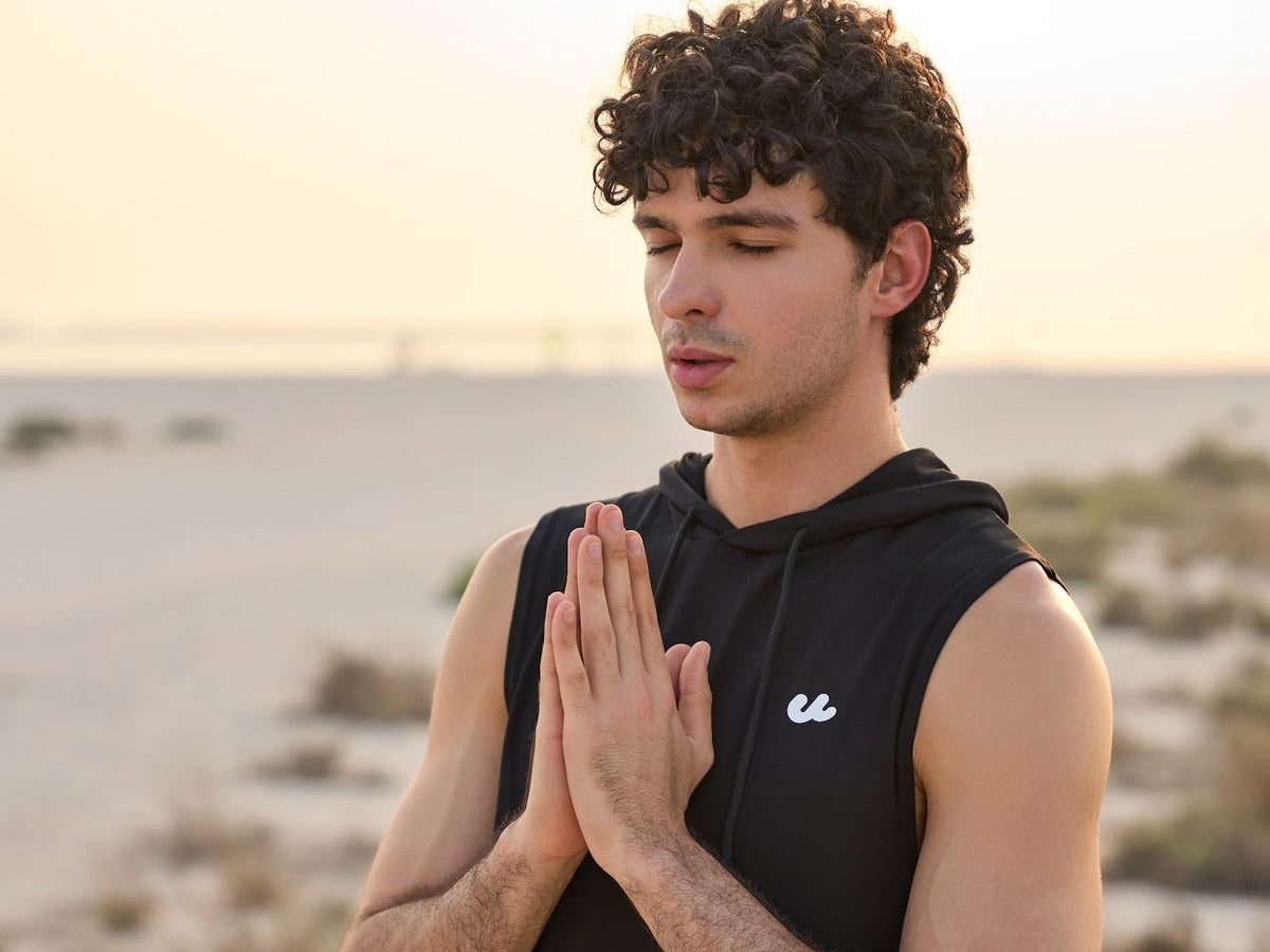 Man in the Urthlete black sleeveless hoodie holding a yoga pose on the beach