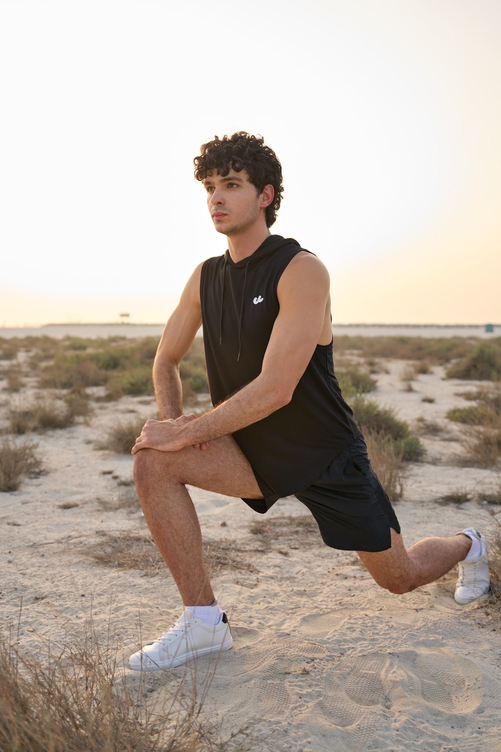 Man in the Urthlete black sleeveless hoodie doing a lunge stretch in the desert