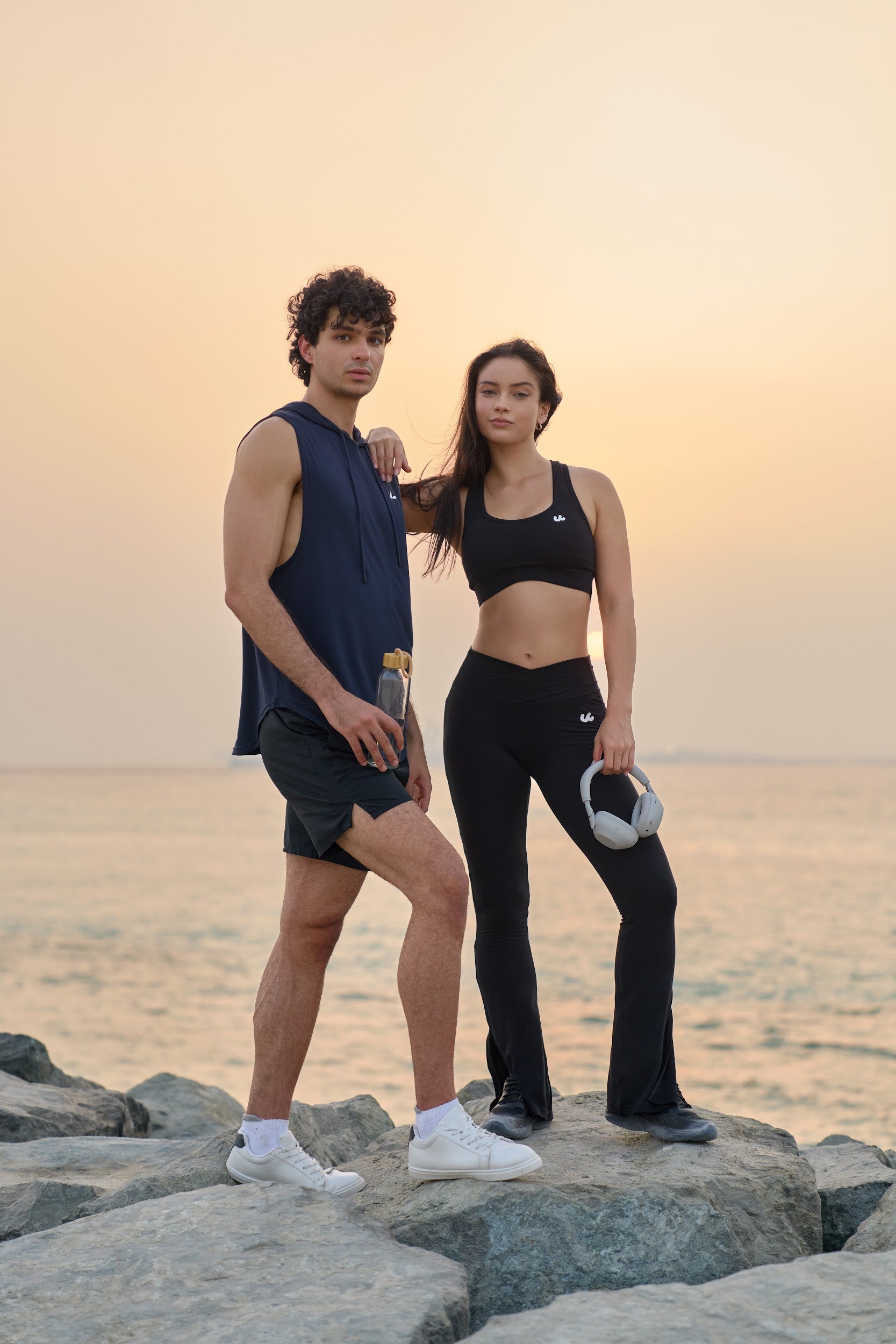 Man and woman standing on rocks by the sea at sunset in Urthlete activewear