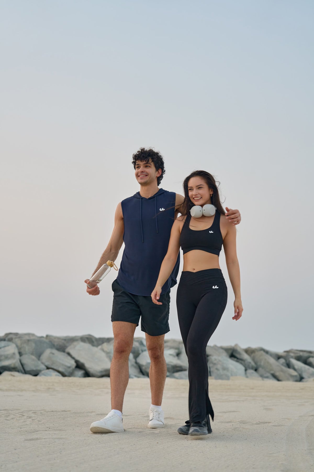 Man and woman walking by the sea in Urthlete sleeveless hoodie, sports bra and flare leggings