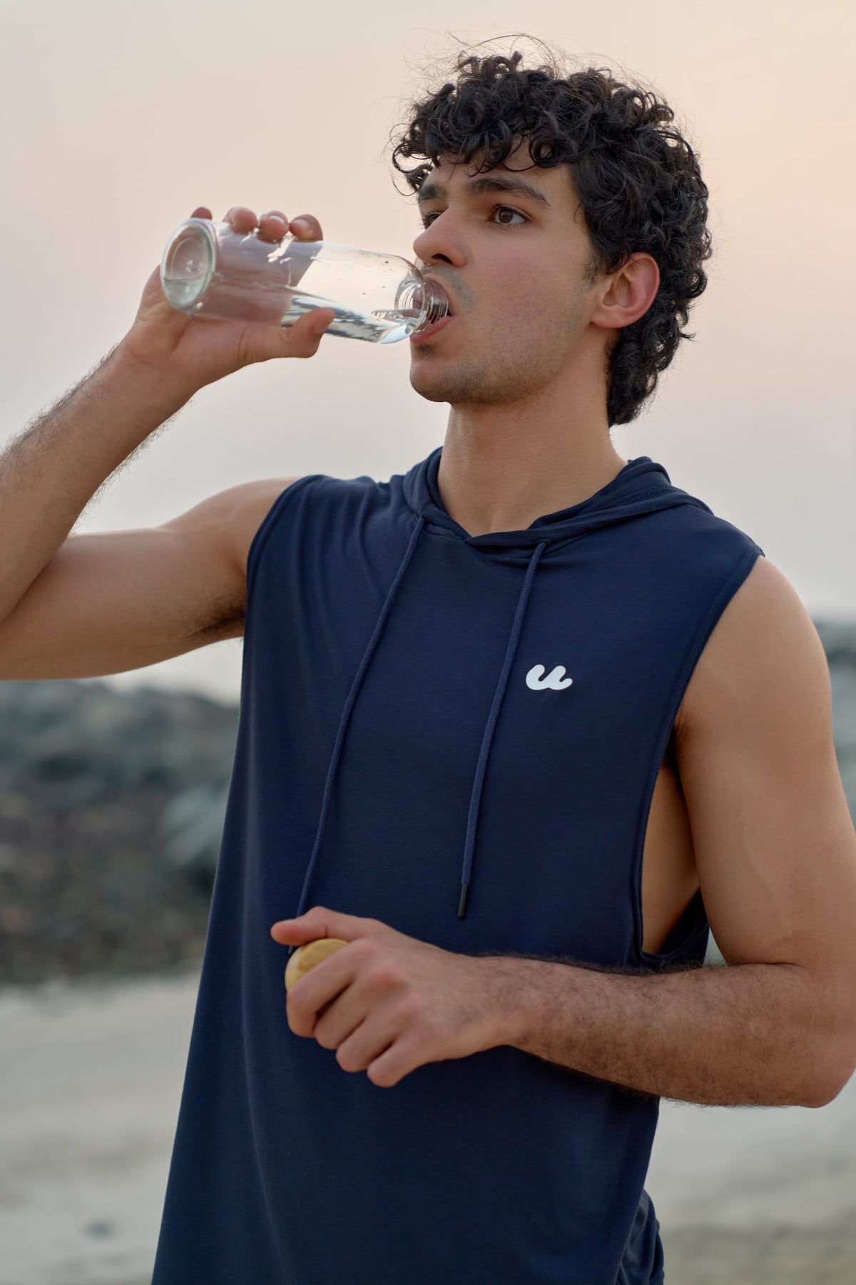 Man drinking water after training in the Urthlete ocean blue sleeveless hoodie